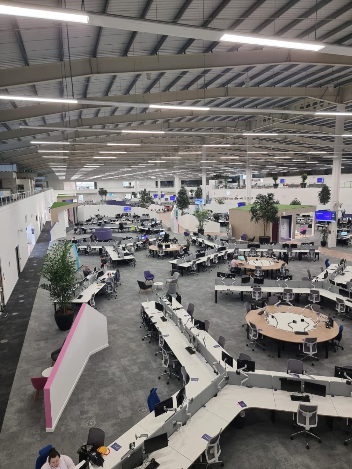 The operational floor from the mezzanine: open-plan desking under the lit roof, pods and partitions complete