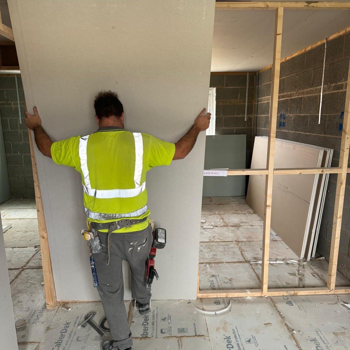 Plasterboard being lifted into place against a timber stud partition on a new build plot