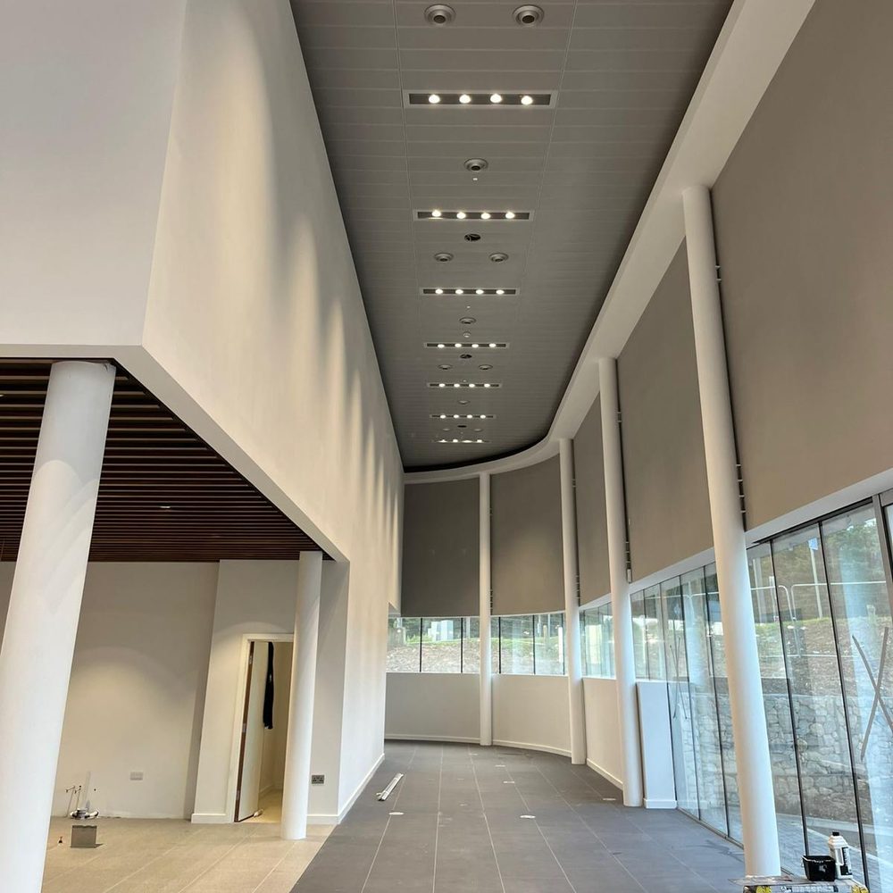 Curved plasterboard bulkhead edging a linear tile ceiling along a glazed corridor