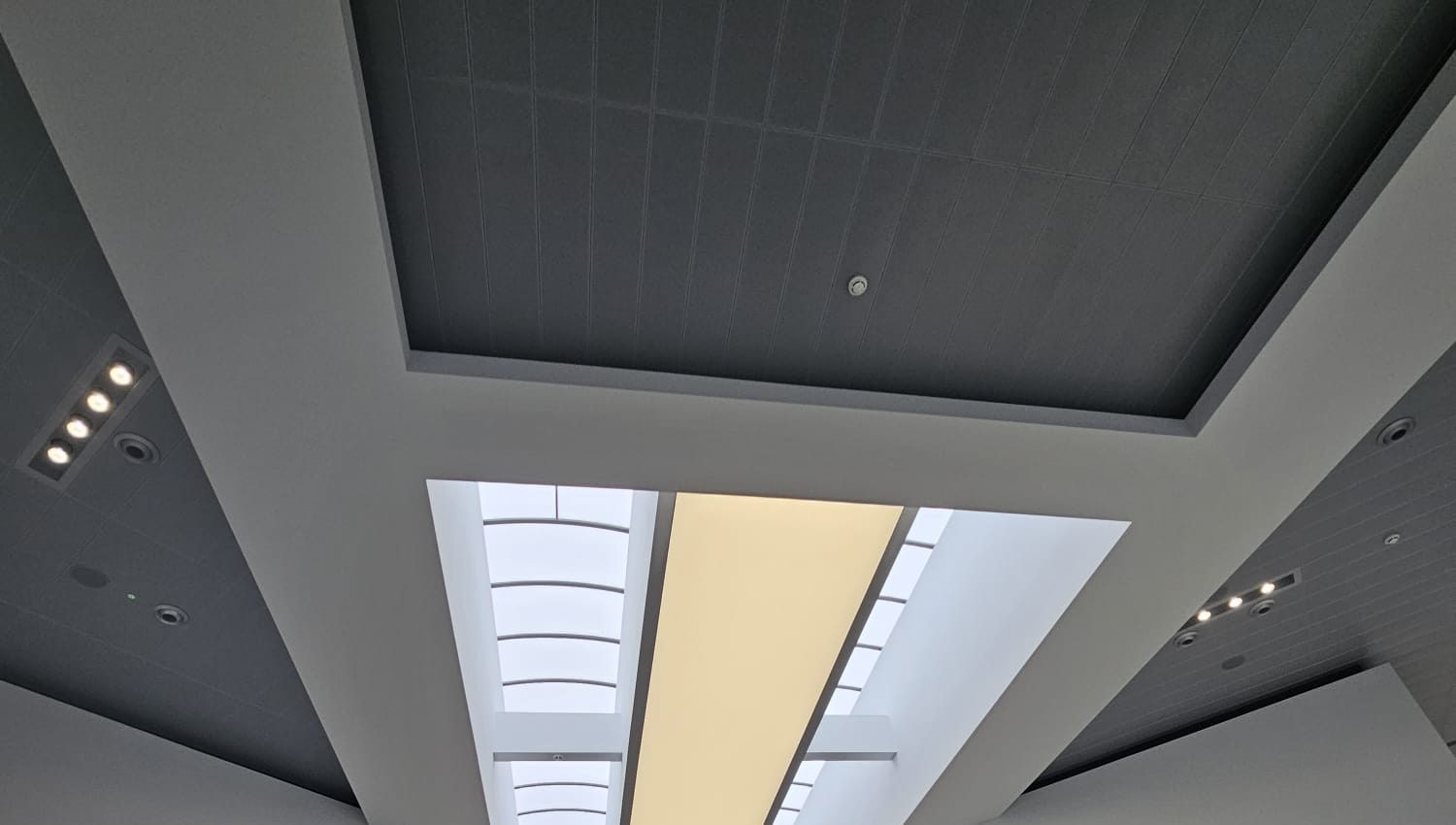 Feature bulkheads framing a rooflight and a lit ceiling panel in a double-height showroom