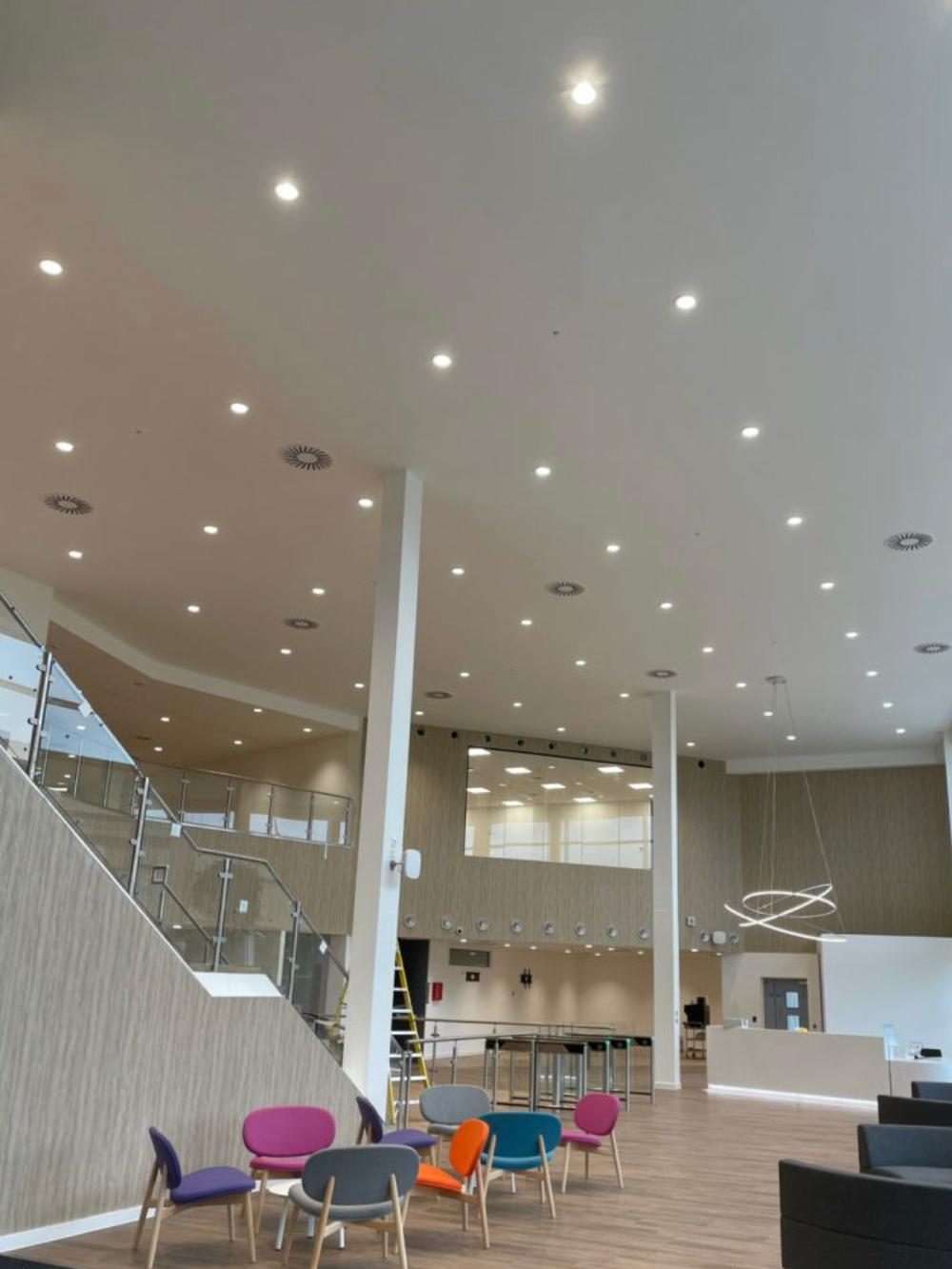 Finished plasterboard ceiling with downlights and bulkheads over a double-height reception