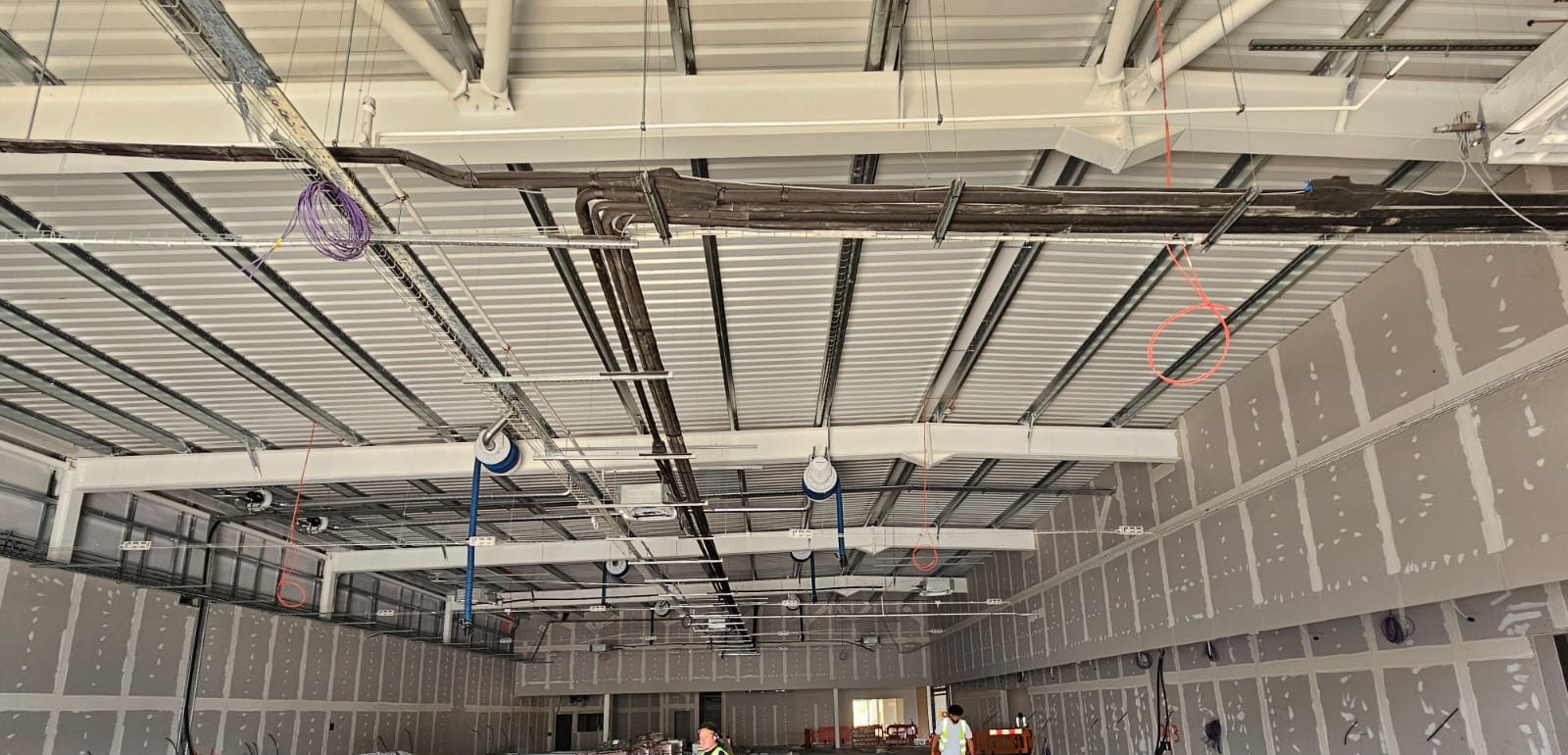 Partition walls boarded, taped and jointed down both sides of a warehouse fit-out, with ceiling hangers and services going in overhead