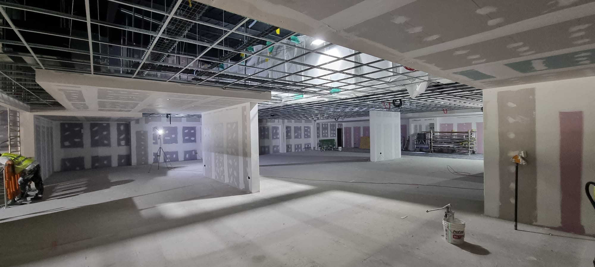 Stud partitions boarded and jointed under an open ceiling grid, with an operative at work
