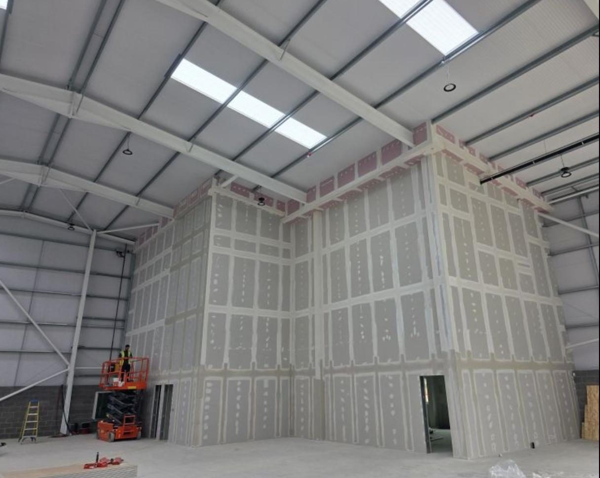 Full-height partitions boarded, taped and jointed up to the roof steels inside a warehouse shell